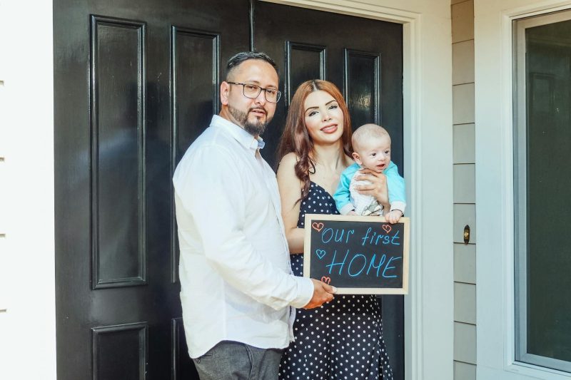 Young family with baby holding a sign Our First Home