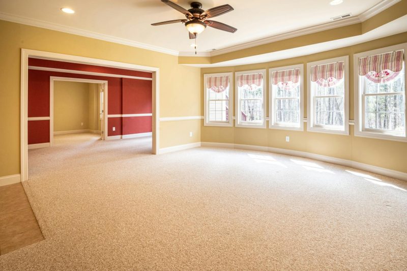 Bright empty room with carpet and ceiling fan ideal for residential