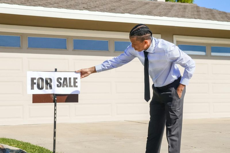 Real estate agent placing a "For Sale" sign in the yard of a suburban house.